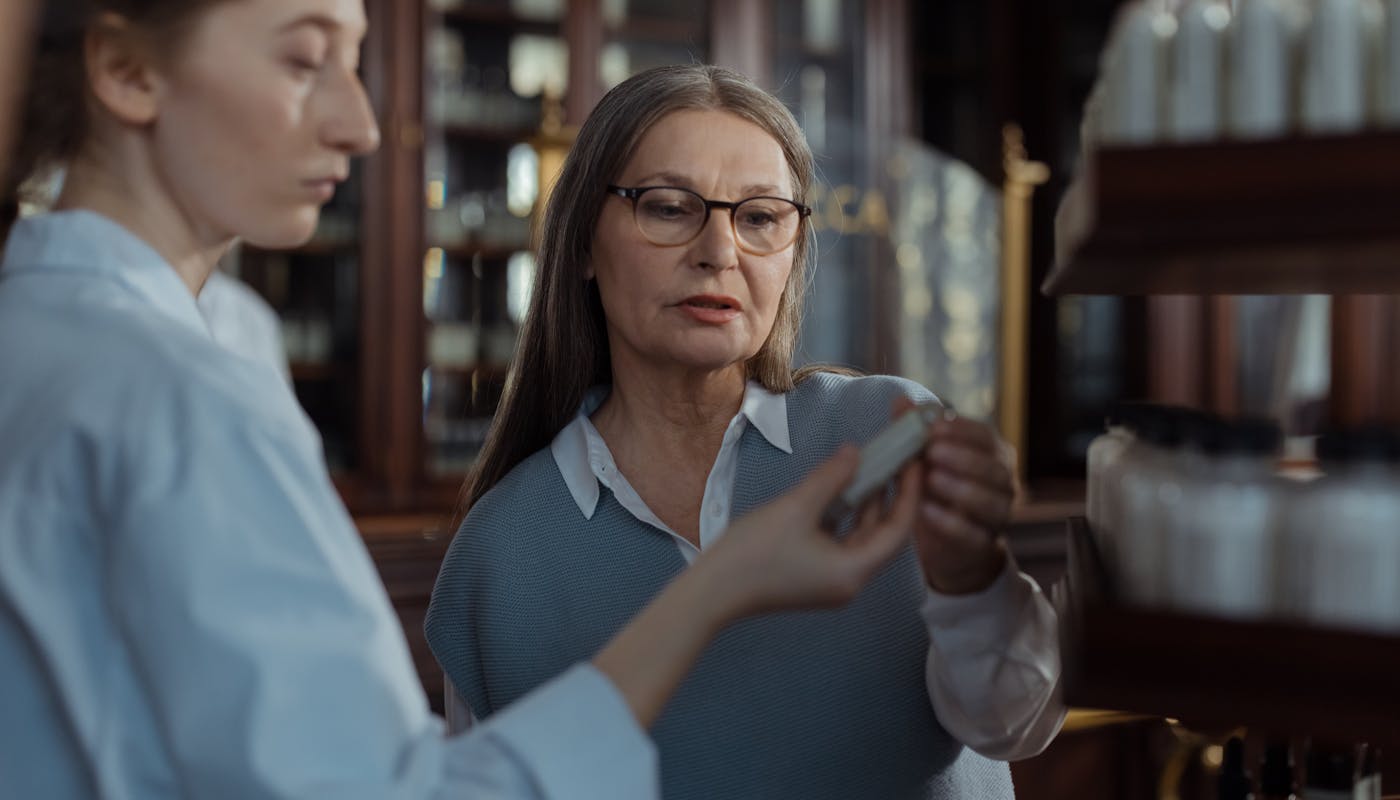 Senior woman discussing prescription medication with a Florida pharmacist at the counter under the new Medicare Part D $2,100 out-of-pocket cap